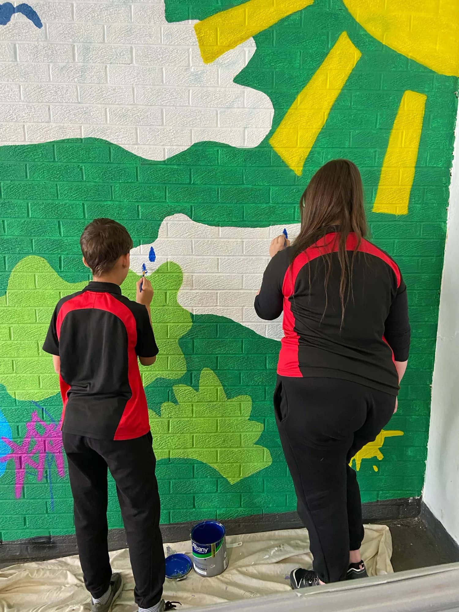 Two young people painting a green mural together